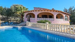 Eine pinkfarbene Villa mit Schwimmbad, Bogenfenstern und einem Balkon mit Geländer.