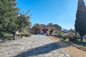 A stone pathway leading to a building with a pink facade, surrounded by greenery and a clear blue sky. - Finca La Solana – Holiday home with a private pool (Jalón)