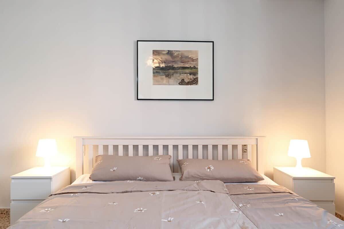 Une chambre à coucher avec un lit, deux tables de chevet et un tableau encadré accroché au mur.