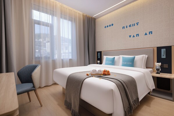 Una habitación de hotel moderna con una cama grande, una mesita de noche, una silla y vistas al exterior a través de cortinas translúcidas.