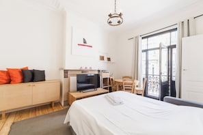 A hotel room with a bed, a TV, a desk, a chair, and a balcony with a view. - 1 Bedroom W Kitchen and Bathroom In Trendy St Gilles (Brussels)
