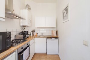 A compact kitchen with white cabinets, a dishwasher, a stove, and a microwave. - 1 Bedroom W Kitchen and Bathroom In Trendy St Gilles (Brussels)