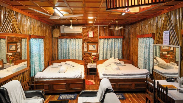 A room with two wooden beds, a ceiling fan, and a wooden wall panel. - Hotel Banalata (Bishnupur)