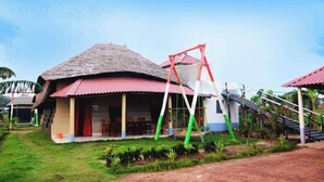A traditional house with a thatched roof, a porch with chairs, and a swing set. - Hotel Banalata (Bishnupur)