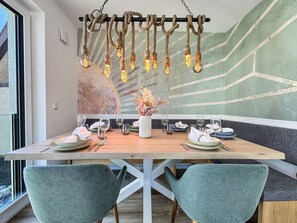 A dining area with a wooden table set for four, a vase with flowers, and a wall with a geometric design. - 5220 - Küstenfeuer - Coastal Lighthouse - 5220 - Luxury - 3 bedrooms - in Dahme with ocean views (Dahme)
