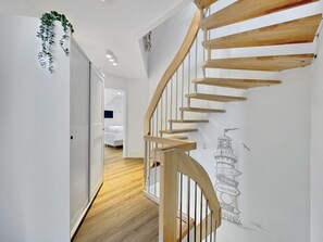 A modern interior with a wooden spiral staircase, a hallway leading to a bedroom, and a wall with a cityscape mural. - 5220 - Küstenfeuer - Coastal fire - 5220 - Luxury - 3 bedrooms - in Dahme with sea view (Dahme)
