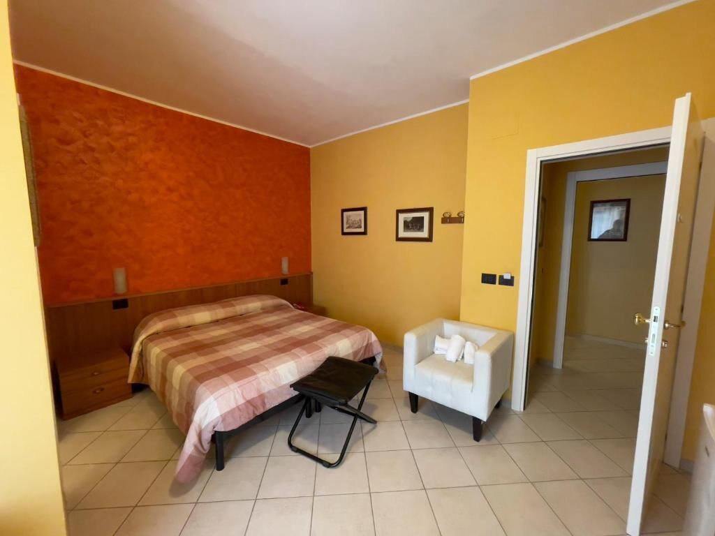Habitación de hotel con cama, una mesita, una silla y una puerta que da a otra estancia.