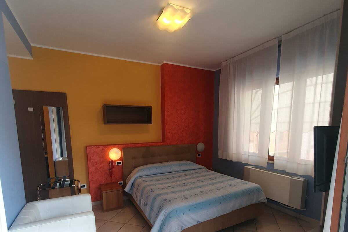 A bedroom with a bed, bedside table, lamp, and a mirror.