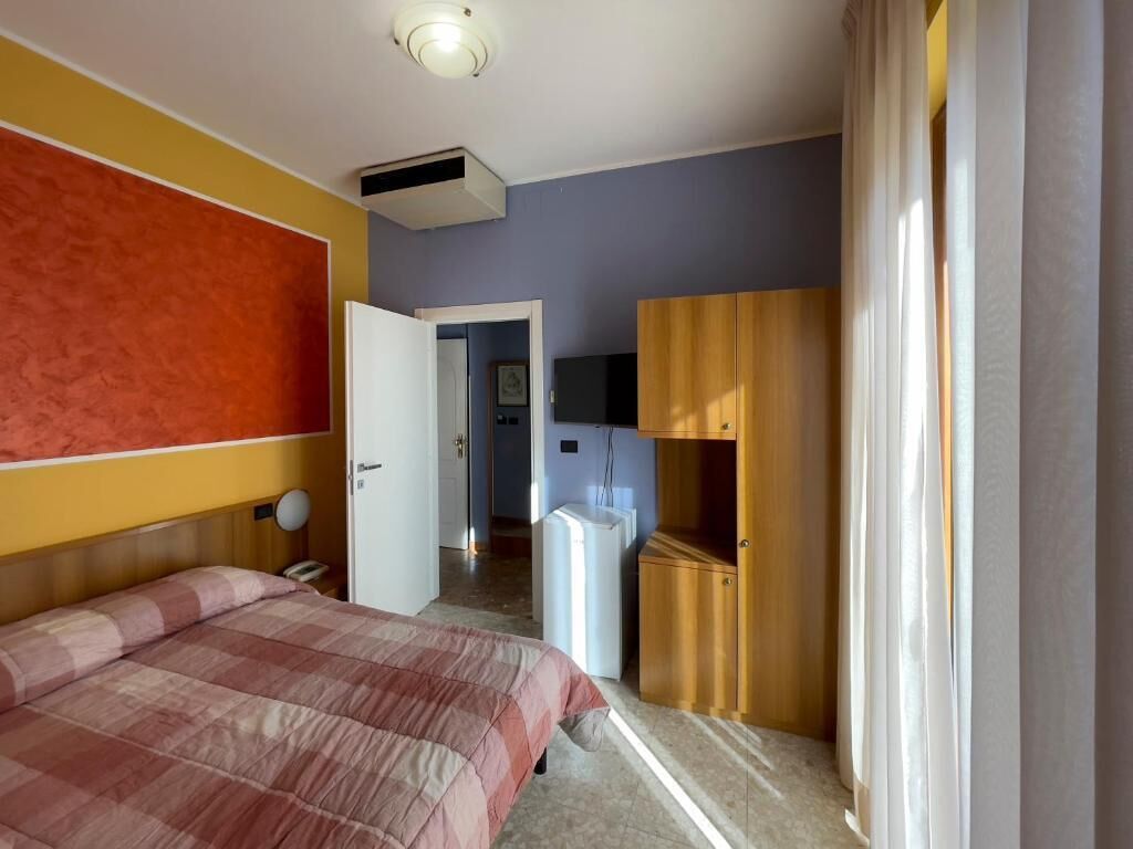 Ein Hotelzimmer mit Bett, Kleiderschrank, Schreibtisch und Fernseher.