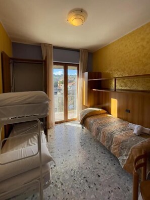 Habitación de hotel con literas, una cama individual, cabecero de madera, luz en el techo y vistas al exterior a través de una puerta corredera.
