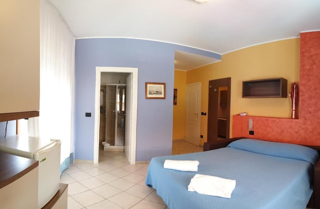 A hotel room with a bed, a desk, a shower, and a television.