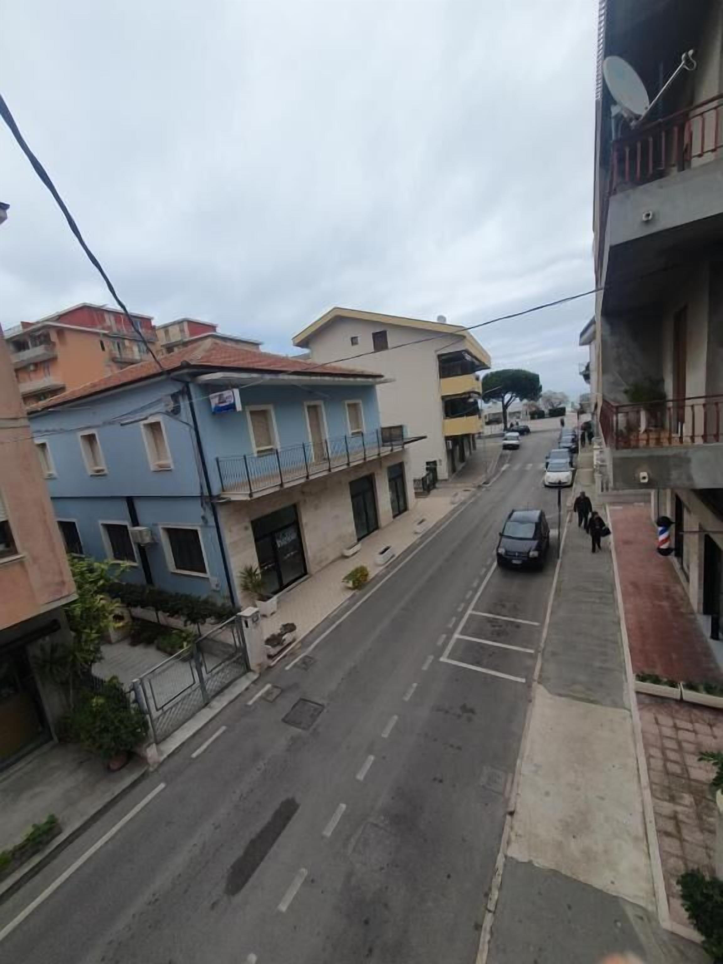 Une vue de rue avec des immeubles, un trottoir et des voitures garées.