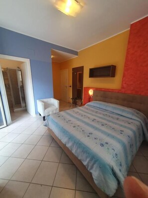 Un dormitorio con cama, una silla, un ventanal corredero y una mesita.