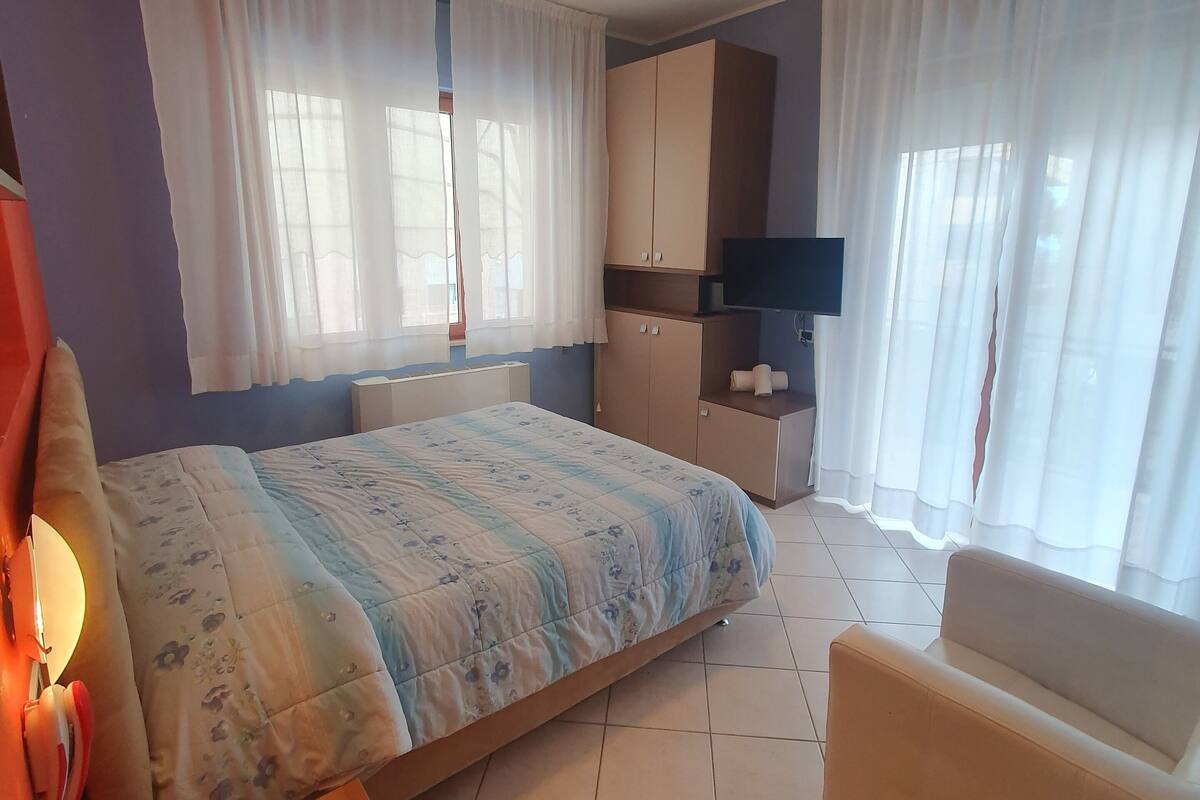 A bedroom with a bed, a chair, a TV, and a wardrobe.