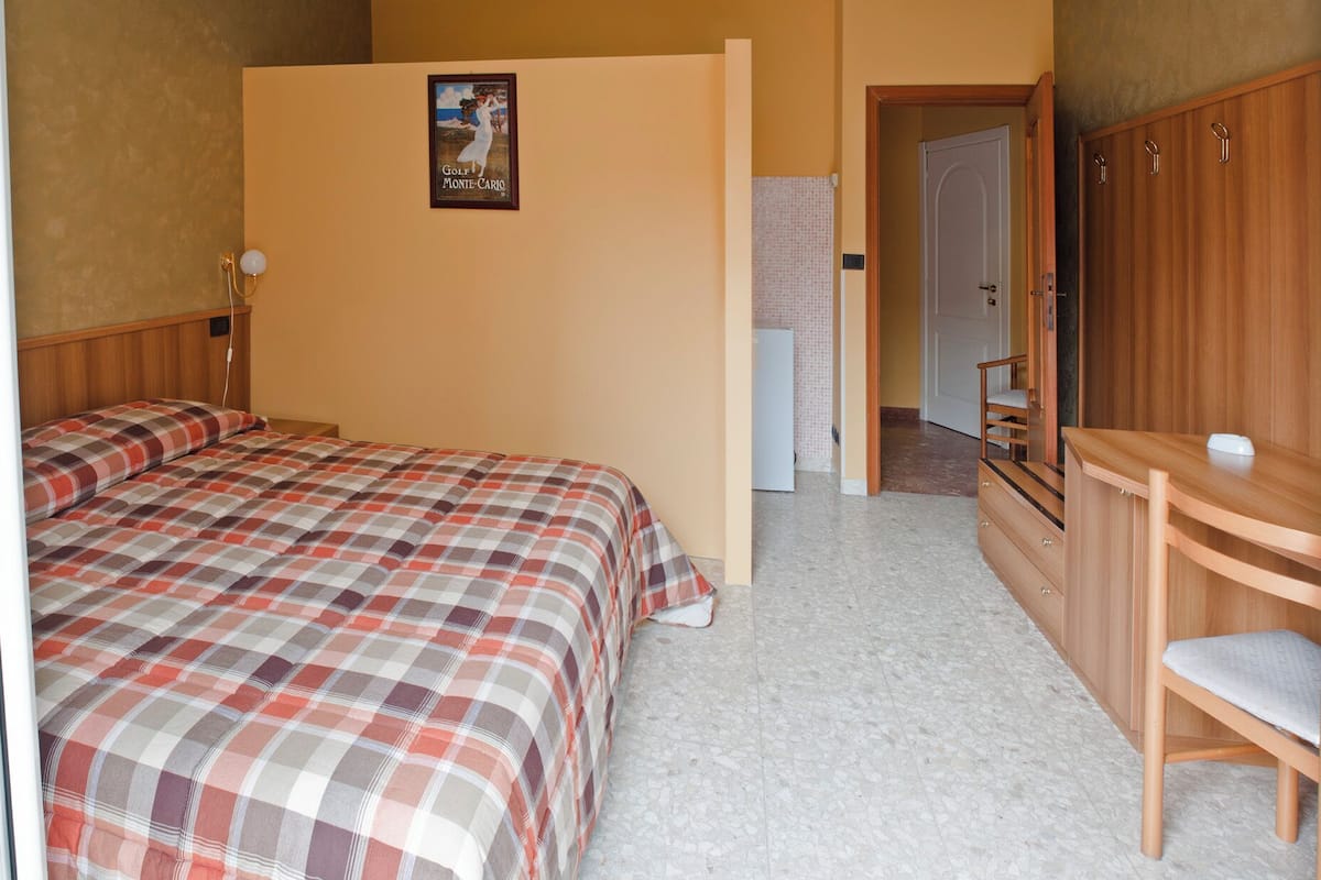 A bedroom with a bed, a wooden wardrobe, a small desk, and a poster on the wall.