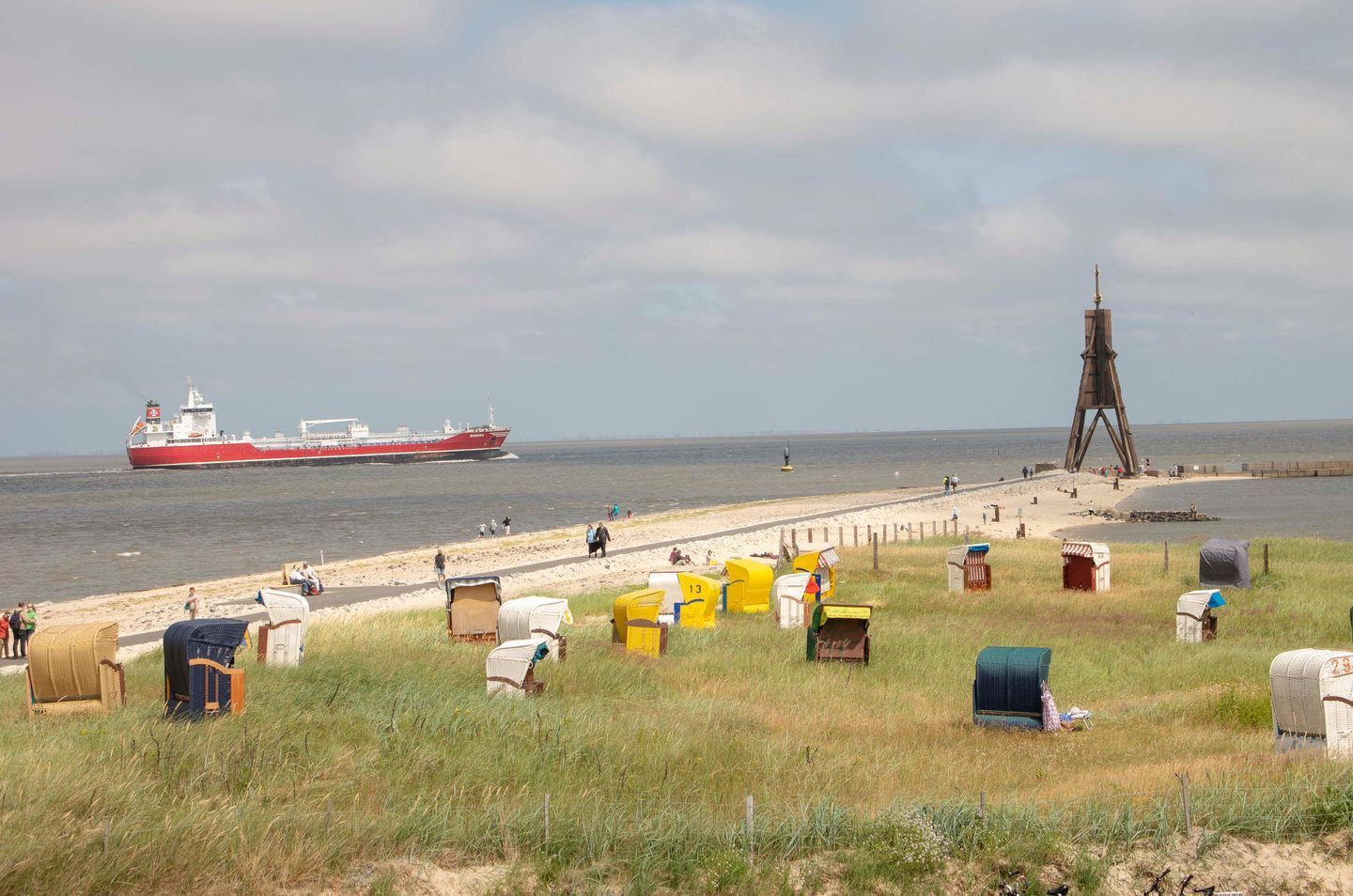 Una playa con un barco grande al fondo, una estructura de madera y varias cabañas de playa numeradas.