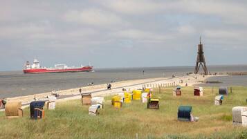 Una playa con un barco grande al fondo, una estructura de madera y varias cabañas de playa numeradas.