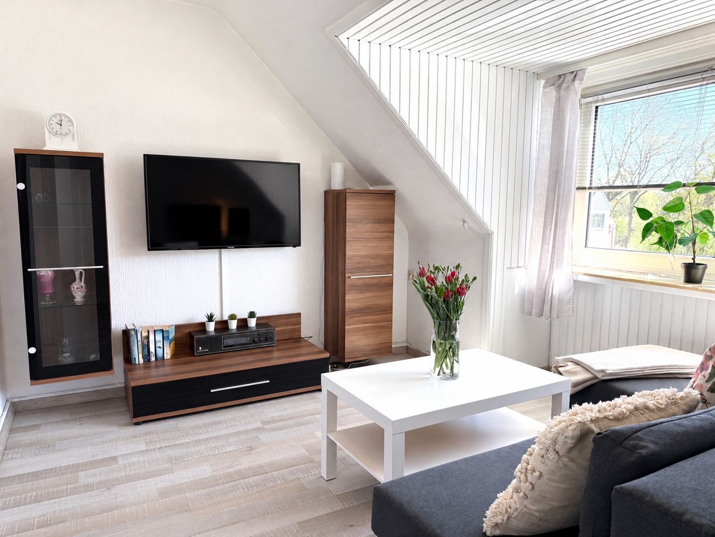 Ein modernes Wohnzimmer mit Flachbildfernseher, Holzschrank und weißem Couchtisch.