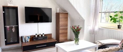 Una sala de estar moderna con un televisor de pantalla plana, un mueble de madera y una mesa de centro blanca.