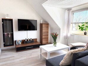 A modern living room with a flat-screen TV, wooden cabinet, and a white coffee table. - Die kleine Cuxperle - Beachfront Vacation Apartment in Cuxhaven - House (Cuxhaven)