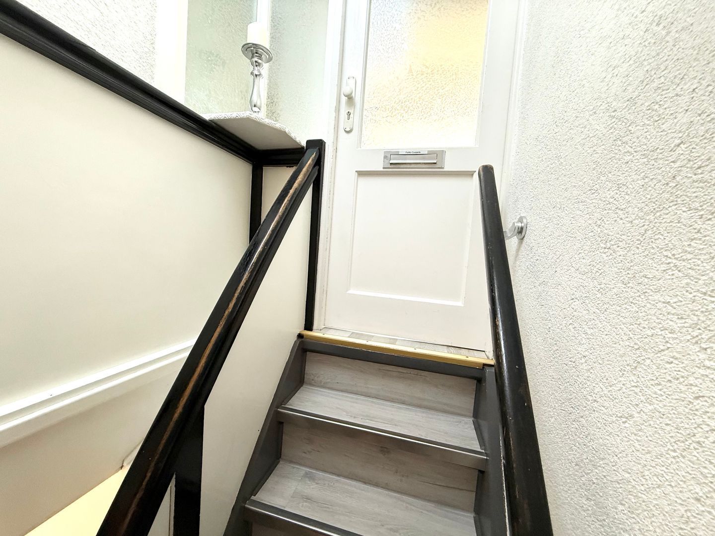 Eine Treppe mit einer weißen Tür am oberen Ende, einer Handläufe und einer strukturierten Wand.
