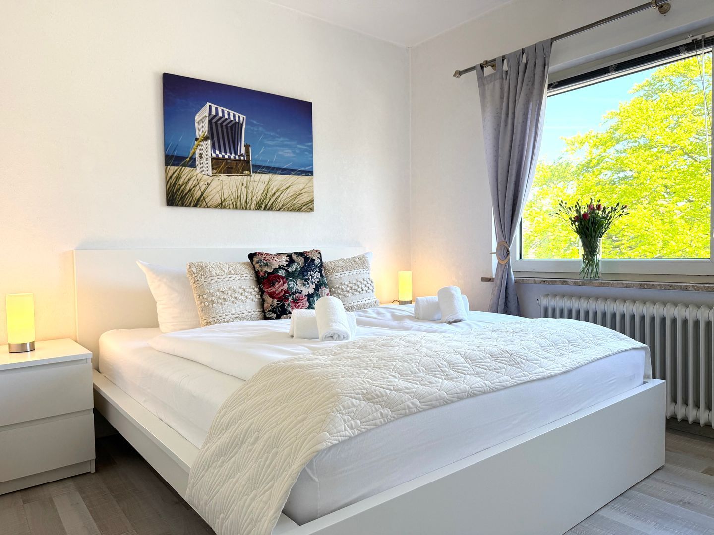 Een hotelkamer met een groot bed, een nachtkastje, een raam met gordijnen en een schilderij aan de muur.