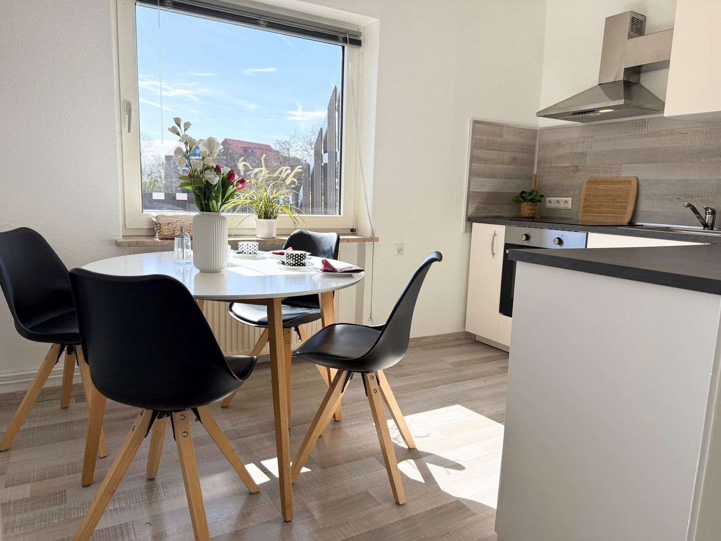 Eine moderne Küche mit Essbereich, ausgestattet mit einem runden Tisch, schwarzen Stühlen, einem Fenster mit Blick und einem eingebauten Herd.