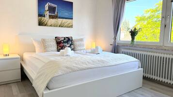 A bedroom with a large bed, two bedside tables, a window with curtains, and a painting on the wall.