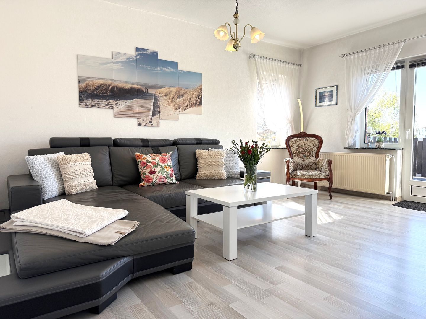 Een moderne woonkamer met een hoekbank, een witte salontafel, een fauteuil met een patroon en een groot raam met gordijnen.