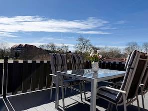 An outdoor patio with a glass table and chairs, a vase with flowers, and a view of a building in the background. - The large Cuxoase - Comfortable vacation apartment with large balcony and close to the beach in (Cuxhaven)