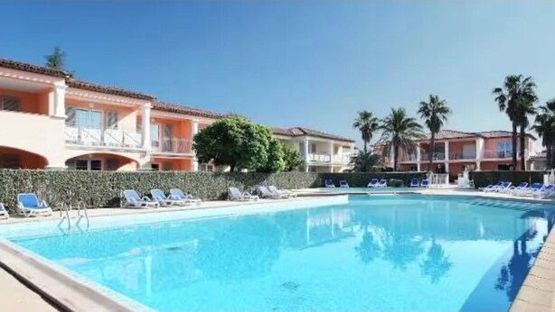 Uma piscina com espreguiçadeiras, um edifício com varandas e palmeiras.