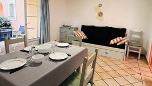 Uma sala de jantar com uma mesa posta para quatro, um sofá com almofadas, um armário e um objeto decorativo na parede.