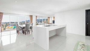 A modern kitchen with a central island, large windows, and a dining area with chairs. - Great Ocean View 2Br Near Beach C265 (Patong)
