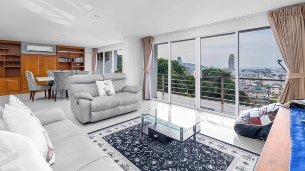 A modern living room with a sofa, a glass coffee table, and a view of the city through large windows. - Great Ocean View 2Br Near Beach C265 (Patong)