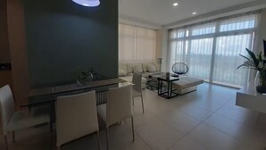 A modern living room with a dining area, large windows, and a ceiling light fixture. - Borneo Holiday Suite @ Riverine Diamond Kuching (Kuching)