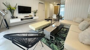 A modern living room with a flat-screen TV, a sofa, a coffee table, and a black chair. - Borneo Holiday Suite @ Riverine Diamond Kuching (Kuching)
