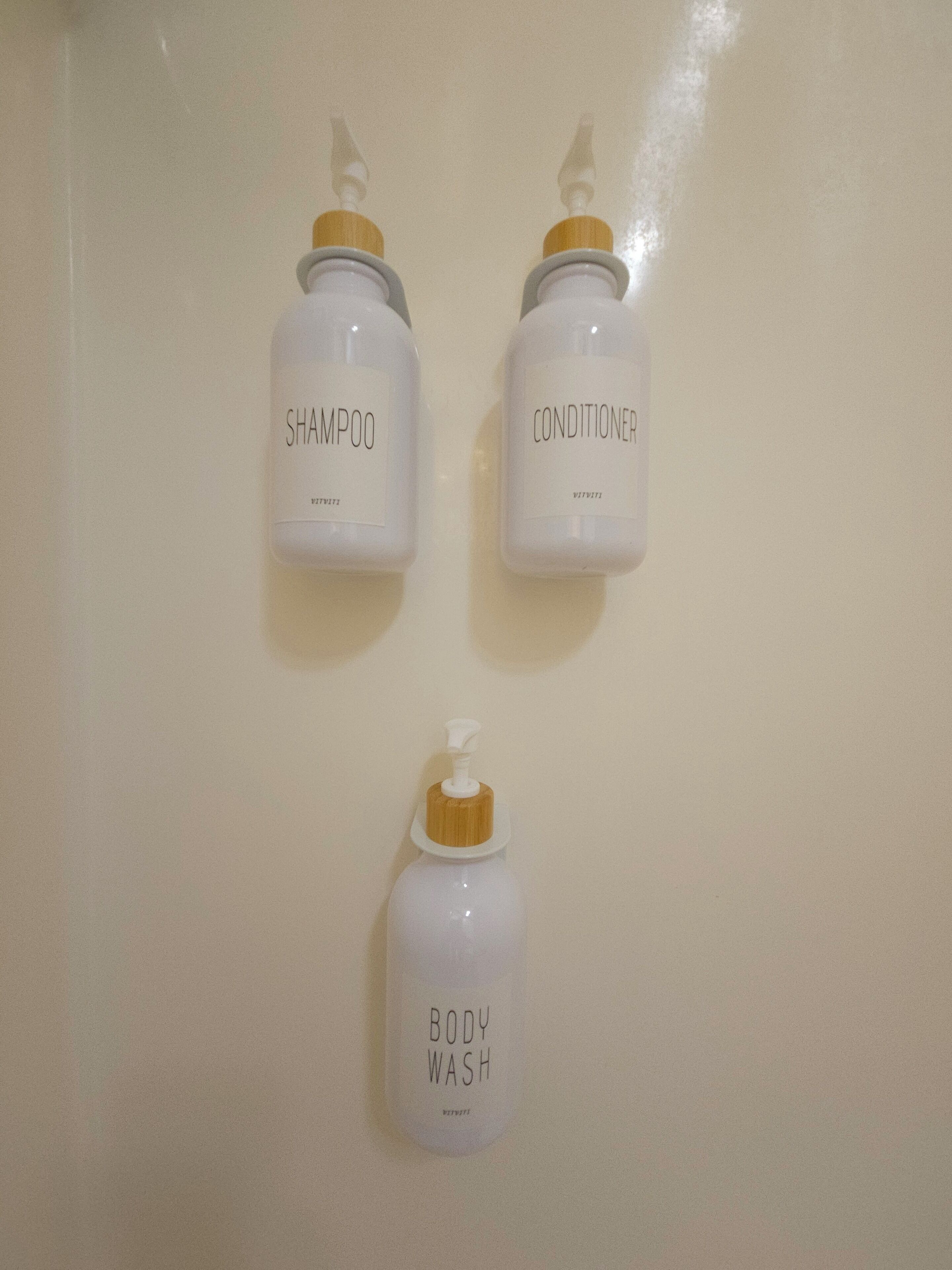 Three bottles of toiletries on a wall: shampoo, conditioner, and body wash.