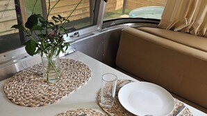 Een gedekte eettafel met borden, bestek en een glas, voorzien van een geweven placemat en een vaas met bloemen erop.
