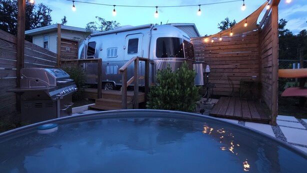 Een achtertuin met een zwembad, een barbecue, een overdekt houten terras en een camper.