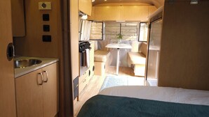 Een ruimtelijk ingerichte camper met een kitchenette, een eethoek en een slaapgedeelte.