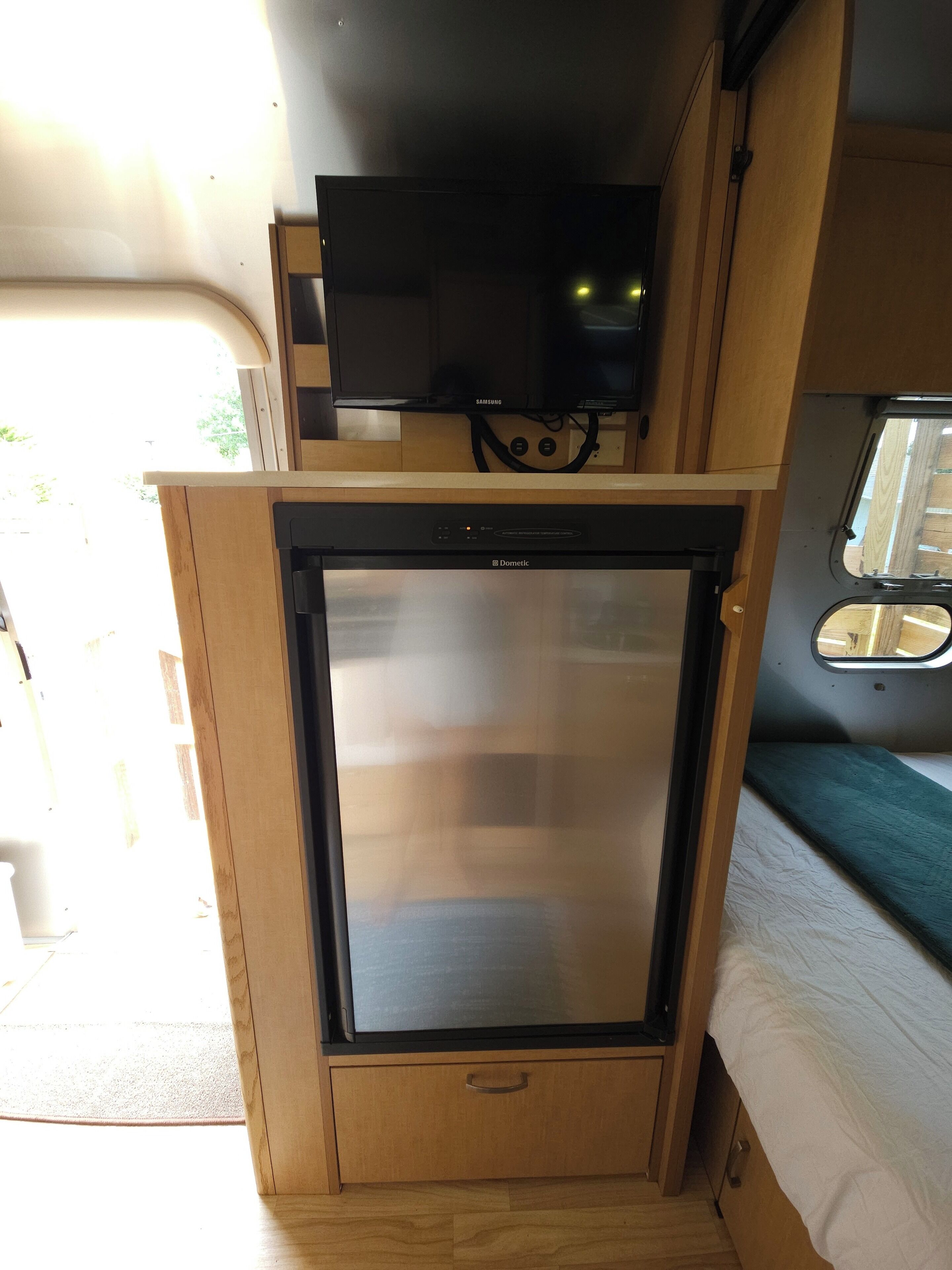 A compact kitchenette with a built-in refrigerator, a small television, and a window for natural light.