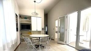 A compact room with a bed, a dining table with chairs, a small kitchen area, and a sliding glass door leading to an outdoor area. - Quiet garden villa just 100mt from the beach (Bibione Pineda)