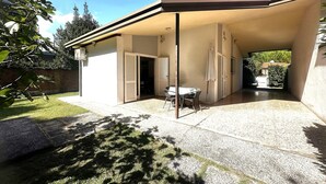 A covered patio with a table and chairs, a sliding door, and a small garden area. - Quiet garden villa just 100mt from the beach (Bibione Pineda)