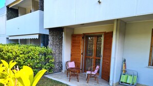 Esterno di un hotel con un portico coperto, due poltrone in vimini, un tavolino e un portaoggetti in metallo verde.