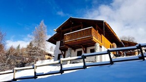 Een houten chalet met balkon, stenen pilaren en een besneeerd landschap.