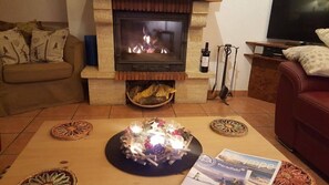 A living room with a stone fireplace, a sofa, a coffee table with decorative items, and a television. - Chalet Beaumont is a spacious yet cosy chalet, just 400 meters from the slopes. (Peisey Vallandry)