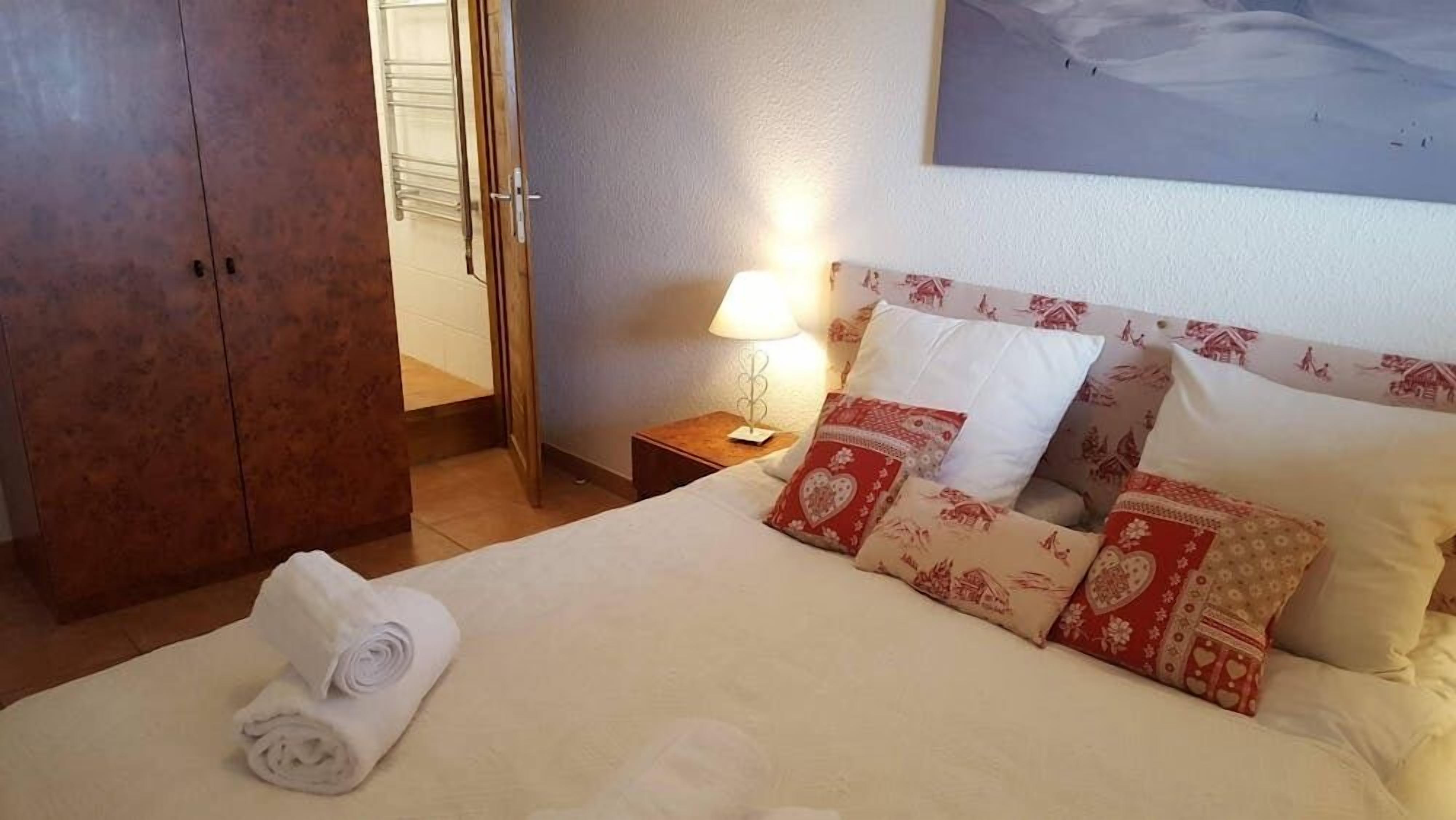 A neatly made bed with patterned pillows, a bedside lamp, and a rolled towel on the floor.