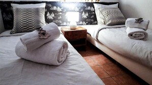 Een hotelkamer met twee bedden, elk met een opgerolde handdoek en een decoratief kussen. Een nachtkastje met een lamp staat tussen de bedden.