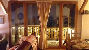 Een knus hoekje met een schuifpui naar een balkon, een houten plafond en een tafeltje met een decoratief tafelkleed.