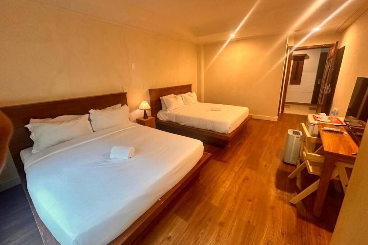 Une chambre d’hôtel avec deux lits, un plancher en bois, un bureau avec une chaise et une petite table.
